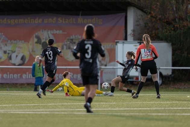21.11.2025, Fußball, 2. Frauen-Bundesliga, 2025 2026, 11. Spieltag, SG 99 Andernach - VfR Schwarz-Weiss Warbeyen 1945 e. V. Lisa Krupp (25 Andernach) erneut zur Stelle. Schiedsrichterin Sarah Willms wirbt mit ihrem Trikot für die EM 2029 - WE29 - Together WE Rise.
