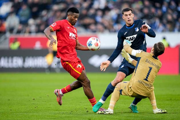 v.li.: Samuel Essende (FCA, 9), Robin Hranac (Hoffenheim, 2), Oliver Baumann (Torwart, Hoffenheim, 1), Zweikampf, Spielszene, Duell, duel, tackle, tackling, Dynamik, Action, Aktion, 29.11.2025, Sinsheim (Deutschland), Fussball, Bundesliga, TSG 1899 Hoffenheim - FC Augsburg, DFB DFL REGULATIONS PROHIBIT ANY USE OF PHOTOGRAPHS AS IMAGE SEQUENCES AND OR QUASI-VIDEO.