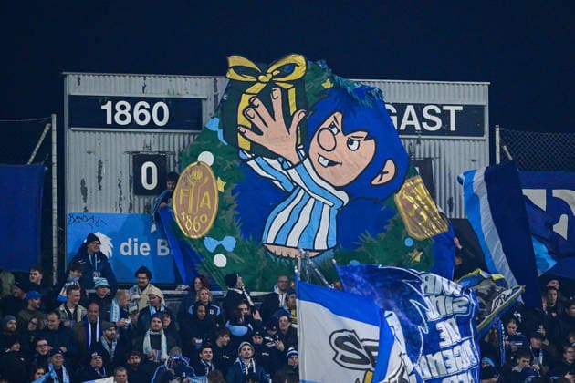 Die Fans des TSV 1860 Muenchen haben einen Pumukel mit blauen Haaren und blau-weissem Trikot vor die Anzeigetafel gehaengt, 20.12.2025, München (Deutschland), Fussball, 3. Liga, TSV 1860 München - SC Verl, DFB DFL REGULATIONS PROHIBIT ANY USE OF PHOTOGRAPHS AS IMAGE SEQUENCES AND OR QUASI-VIDEO.