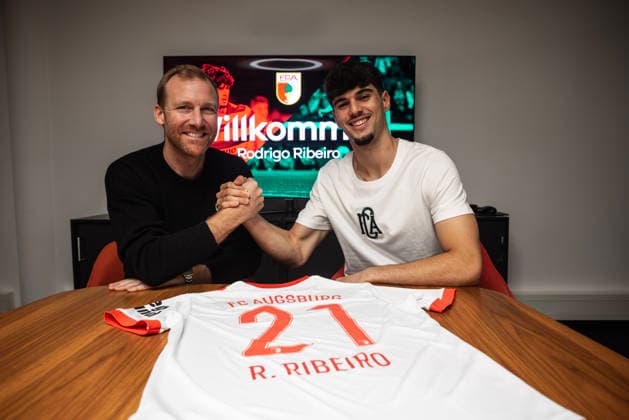 15.01.2026, GER, Fussball, Herren, FC Augsburg, 1. BL, Saison 2025 2026, Neuzugang, Verplfichtung, Transfer, Ribeiro FCA-Sportdirektor Benni Weber (li.) und Neuzugang Rodrigo Ribeiro klatschen ein. Vor ihnen liegt das Trikot mit der Nummer 21. Augsburg