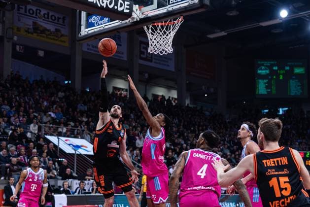 Spielaktion mit Tommy Kuhse (12; Rasta Vechta) wirftt und Jalen Finch (0, Telekom Baskets Bonn) verteidigt unter dem Korb im Spiel zwischen Telekom Baskets Bonn und RASTA Vechta am 21. Spieltag der EasyCredit BBL in Bonn. Tommy Kuhse (12; Rasta Vechta) wirftt und Jalen Finch (0, Telekom Baskets Bonn) verteidigt