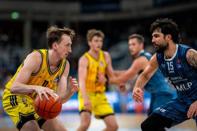 Szene mit Marcel Keßen (15; MLP Academics Heidelberg) in blauem Trikot, der gegen Moses Wood (11; Alba Berlin) mit Ball und Jwan Roberts (13; Alba Berlin) in gelben Trikots verteidigt easyCredit BBL: MLP Academics Heidelberg – Alba Berlin - 06.03.2026