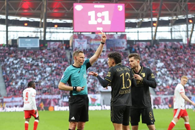 1. Fußball Bundesliga: RB Leipzig - FC Augsburg; 07.03.2026 Schiedsrichter Martin Petersen zeigt Dimitris Giannoulis (13, FC Augsburg) die Gelbe Karte, Verwarnung. Im Hintergrund die Videowand mit dem Spielstand von 1:1-Unentschieden. LEIPZIG, DEUTSCHLAND - MARCH 7: Bundesliga-Spiel RB Leipzig - FC Augsburg in der Red Bull Arena am 25. Spieltag der 1. Bundesliga am March 7, 2026 in Leipzig, Deutschland. DFL REGULATIONS PROHIBIT ANY USE OF PHOTOGRAPHS AS IMAGE SEQUENCES AND OR QUASI-VIDEO.
