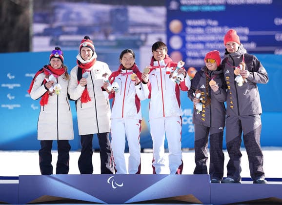 (260308) -- TESERO, March 8, 2026 -- Gold medalist Wang Yue (3rd L) and her guide Chen Guoming (3rd R) of China pose on the podium with silver medalist Carina Edlingerova (1st L) and guide Alexandr Patava (2nd L) of the Czech Republic and bronze medalist Leonie Maria Walter (2nd R) and guide Christian Krasman of Germany after the women s sprint vision impaired final of para biathon at the Milan-Cortina 2026 Paralympic Winter games, Winterspiele,Spiele, Summer games in Tesero, Italy, March 7, 2026. ) (SP)ITALY-TESERO-PARALYMPIC WINTER GAMES-PARA BIATHLON-WOMEN S SPRINT VISION IMPAIRED HouxZhaokang 