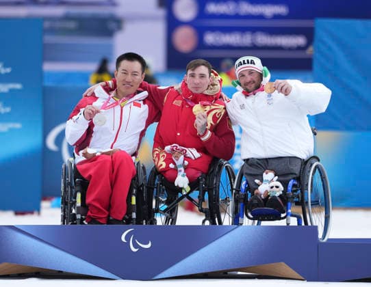 (260315) -- TESERO, March 15, 2026 -- Gold medalist Ivan Golubkov (C) of Russia, silver medalist Mao Zhongwu (L) of China, bronze medalist Gluseppe Romele of Italy pose during the awarding ceremony for the para cross-country skiing men s 20km interval start sitting at the Milan-Cortina 2026 Paralympic Winter games, Winterspiele,Spiele, Summer games in Tesero, Italy, March 15, 2026. ) (SP)ITALY-TESERO-PARALYMPIC WINTER GAMES-PARA CROSS-COUNTRY SKIING-MEN S 20KM INTERVAL START SITTING HouxZhaokang 