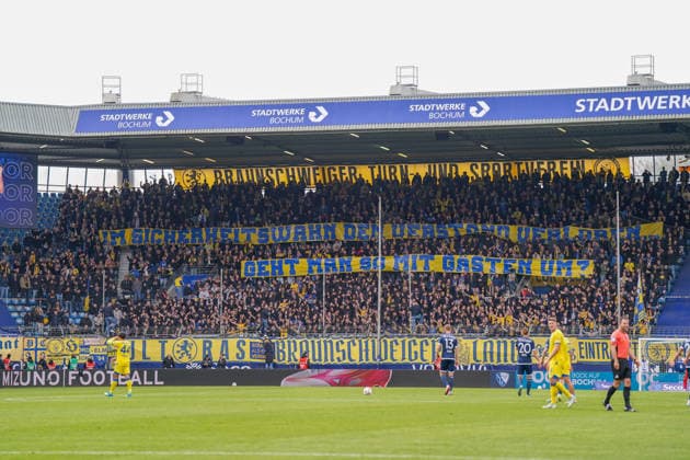 Deutschland: Fussball 2. Bundesliga 2025 - 2026, 29. Spieltag - VfL Bochum vs Eintracht Braunschweig - Vonovia Ruhrstadion: Bochum, Deutschland, Europa, Gaesteblock, Fans, Zuschauer, Menschenmenge, Fankurve, Auswaertsfans, Choreographie, Banner, Spruchband Im Sicherheitswahn den Verstand verloren geht man so mit Gaesten um?, Protest, Kritik, Fankultur, Stimmung, Atmosphaere, Tribuene, Totale, Innenansicht, Sportstaette, Vereinsfarben Gelb Blau, Zaunfahnen, Fahnen, Support, Wettbewerb, Profiliga, Spielszene, Spieler im Vordergrund, Schiedsrichter, Spielfeld, Rasen