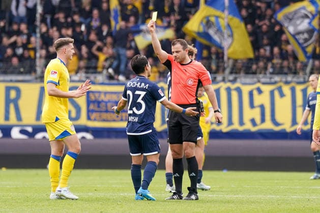 Deutschland: Fussball 2. Bundesliga 2025 - 2026, 29. Spieltag - VfL Bochum vs Eintracht Braunschweig - Vonovia Ruhrstadion: Schiedsrichter Wolfgang Haslberger zeigt Koji Miyoshi (VfL Bochum, 23) die Gelbe Karte