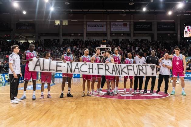 Kur Jongkuch (15; Telekom Baskets Bonn), Michael Kessens (6; Telekom Baskets Bonn), Alijah Comithier (2; Telekom Baskets Bonn), Melvin Jostmann (12; Telekom Baskets Bonn), Patrick Heckmann (33; Telekom Baskets Bonn), Tylan Birts (5; Telekom Baskets Bonn) und Jalen Finch (0; Telekom Baskets Bonn) präsentieren gemeinsam ein Banner mit der Aufschrift ALLE NACH FRANKFURT! in der TelekomDome Arena EasyCredit BBL Ligaspiel am 29. Spieltag in Bonn zwischen Telekom Baskets Bonn und Basketball Löwen Braunschweig. Mannschaft von Kur Jongkuch (15; Telekom Baskets Bonn) mit Banner