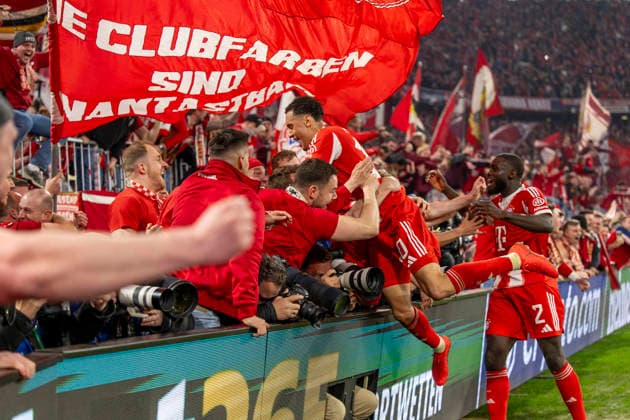 15.04.2026, Fussball UEFA Championsleague 2025 2026: Viertelfinale Rückspiel, FC Bayern München - Real Madrid, in der Allianz-Arena München, Fans stürmen vor Abpfiff den Innenraum und drücken beim Torjubel die Banden mit den Fotografen um, zwei Fotografen werden verletzt, sogar bewusstlos, und müssen danach nötärztlich versorgt werden. Jamal Musiala (Bayern München) springt auf das Menschenknäuel. re: Dayot Upamecano (FC Bayern München)