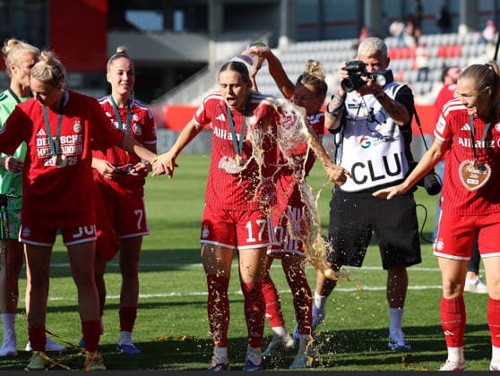 Fussball, Frauen, Google Pixel Frauen Bundesliga, 25.Spieltag, Saison 2025 2026, FC Bayern München - Eintracht Frankfurt, Campus Die Meisterfeier nach dem Spiel, hier die Mannschaft des FC Bayern München Frauen, hier Bierdusche von Linda Dallmann (FC Bayern München) (re.) auf Klara Bühl Buehl (FC Bayern München) (li.)