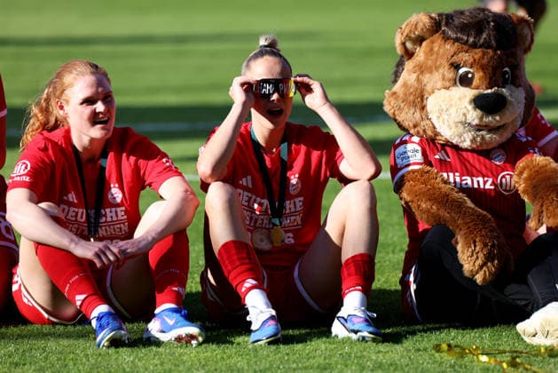 Fussball, Frauen, Google Pixel Frauen Bundesliga, 25.Spieltag, Saison 2025 2026, FC Bayern München - Eintracht Frankfurt, Campus Die Meisterfeier nach dem Spiel, hier die Mannschaft des FC Bayern München Frauen, hier sitzend Stine Ballisager (FC Bayern München) Jovana Damnjanovic (FC Bayern München) mit Champions Brille und dem Maskottchen (v.l.n.r.)