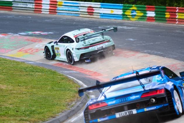 Der mintfarbene Porsche 911 GT3 mit der Startnummer 24 von Lionspeed GP gerät beim Durchfahren einer Kurve auf dem Nürburgring auf den Randstein und wirbelt Staub auf. Die Sponsoren H&R und Wempe sind auf der Karosserie deutlich erkennbar. Im Vordergrund ist das Heck eines blauen Audi ebenfalls auf der Nordschleife zu sehen. Laurens Vanthoor & Laurin Heinrich & Ricardo Feller (Lionspeed GP) Porsche 911 GT3 24 von Lionspeed GP in der Kurve am Nürburgring