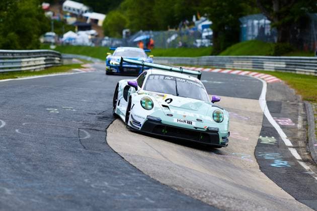 Der Porsche 911 GT3 R Lukas Ertl & Matthias Benndorf & Maximilian Johannes Ertl & Stefan Ertl (Reiter Engineering) von Reiter Engineering durchfährt eine enge Kurve auf der Nordschleife des Nürburgrings. Das in Mintgrün gehaltene Fahrzeug mit den markanten lila Akzenten und dem Gran Turismo-Sponsoring trägt gut sichtbar die Startnummer 91 sowie den H&R- und Michelin-Schriftzug. Im Hintergrund folgt ein weiteres GT3-Fahrzeug in blauer Lackierung. Porsche 911 GT3 R 91 von Reiter Engineering in der Nordschleife-Kurve