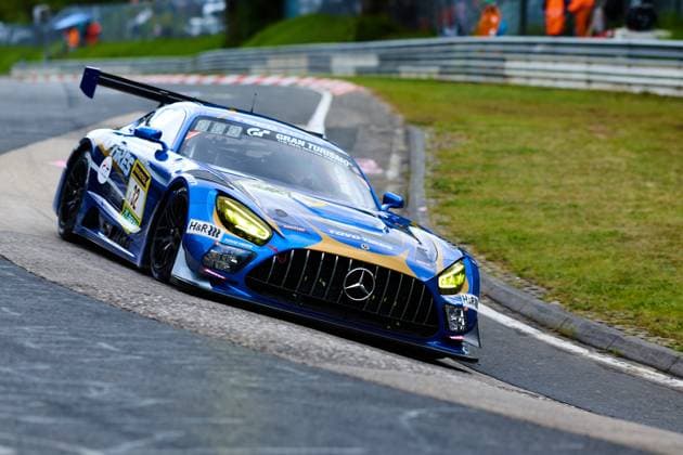 Der Mercedes-AMG GT3 mit der Startnummer 32 des Teams Toyo Tires with Ring Racing durchfährt eine Kurve auf dem Nürburgring. Das in Blau und Gold gehaltene Fahrzeug Andreas Gülden & Tim Sandtler & Yuichi Nakayama (Toyo Tires with Ring Racing) trägt die Sponsoren Toyo Tires, H&R und Gran Turismo prominent auf der Karosserie. Die gelb leuchtenden Scheinwerfer und der dynamische Anpressdruck-Heckflügel unterstreichen den Renncharakter des GT3-Boliden beim ADAC RAVENOL 24h Nürburgring 2026. Mercedes-AMG GT3 32 von Toyo Tires with Ring Racing auf der Nordschleife