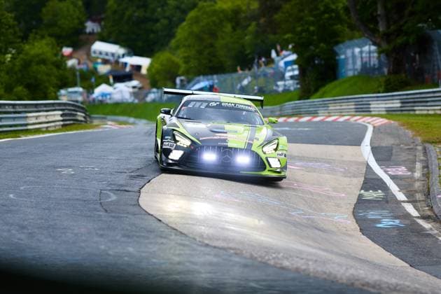 Der Mercedes-AMG GT3 mit der Startnummer 80 des Teams Mercedes-AMG Team RAVENOL durchfährt mit eingeschalteten Scheinwerfern eine enge Kurve auf der Nordschleife des Nürburgrings. Das markant grün-schwarz lackierte Fahrzeug Fabian Schiller & Luca Stolz & Maro Engel & Maxime Martin (Mercedes-AMG Team RAVENOL) trägt Sponsoren wie RAVENOL, Gran Turismo, H&R und Goodyear und setzt sich dynamisch in Szene vor dem typischen Streckenpanorama der Eifel. Mercedes-AMG GT3 80 von Mercedes-AMG Team RAVENOL auf der Nordschleife