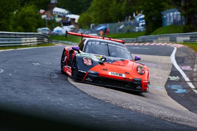 Der Porsche 911 GT3 mit der Startnummer 91 von Reiter Engineering durchfährt eine enge Kurve auf der Nordschleife des Nürburgrings. Das in leuchtendem Orange-Schwarz gehaltene Fahrzeug Lukas Ertl & Matthias Benndorf & Maximilian Johannes Ertl & Stefan Ertl (Reiter Engineering) trägt die Sponsoren H&R, ABACUS und Gran Turismo und zeigt die typischen Leitplanken und Curbs der berühmten Rennstrecke in der Eifel. Porsche 911 GT3 91 von Reiter Engineering in der Nordschleife-Kurve