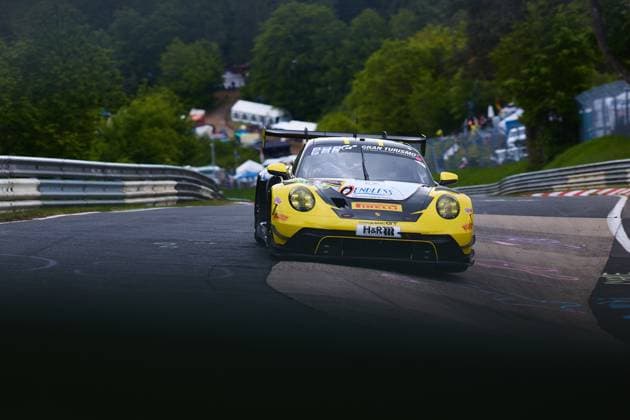 Der gelb-schwarze Porsche 911 GT3 Bastian Buss & Michael Christensen & Michael Klitgaard Christensen (Dinamic GT) von Dinamic GT durchfährt eine Kurve auf der Nordschleife des Nürburgrings. Das Fahrzeug trägt die Sponsoren H&R, Pirelli und Endless und ist mit Gran-Turismo-Branding versehen. Im Hintergrund sind die typischen grünen Hügel der Eifel sowie Zuschauer am Streckenrand zu sehen. Porsche 911 GT3 von Dinamic GT auf der Nordschleife