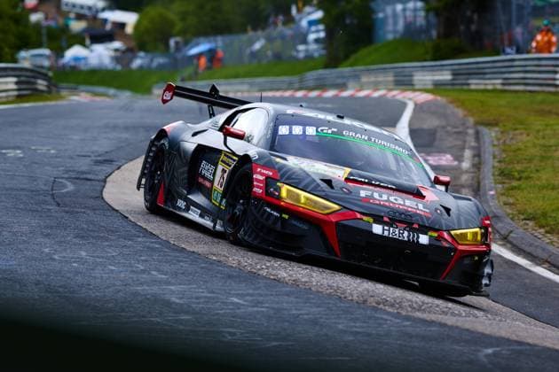Der Audi R8 LMS GT3 mit der Startnummer 75 von Falken Motorsports durchfährt eine enge Kurve auf der Nordschleife des Nürburgrings. Das dunkelgraue Fahrzeug Benjamin Leuchter (Falken Motorsports) mit markanten gelben LED-Scheinwerfern und rotem Farbakzent trägt die Sponsoren Falken, Fugel Gruppe und H&R prominent auf der Karosserie. Im Hintergrund sind Zuschauer und die typische Vegetation der Eifel zu erkennen. Audi R8 LMS GT3 75 von Falken Motorsports auf der Nordschleife