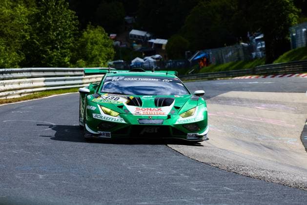 Der Lamborghini Huracán GT3 mit der Startnummer 130 des Red Bull Team ABT (Marco Mapelli & Nicholas Yelloly & Nicky Catsburg (Red Bull Team ABT)) durchfährt eine Kurve auf der Nordschleife des Nürburgrings. Das in leuchtendem Grün gehaltene Fahrzeug trägt die Sponsoren Schaeffler, SONAX Müller und Gran Turismo auf der Karosserie. Im Hintergrund sind die typischen rot-weißen Curbs sowie das bewaldete Streckenprofil der Nordschleife zu erkennen. Lamborghini Huracán GT3 130 von Red Bull Team ABT auf der Nordschleife