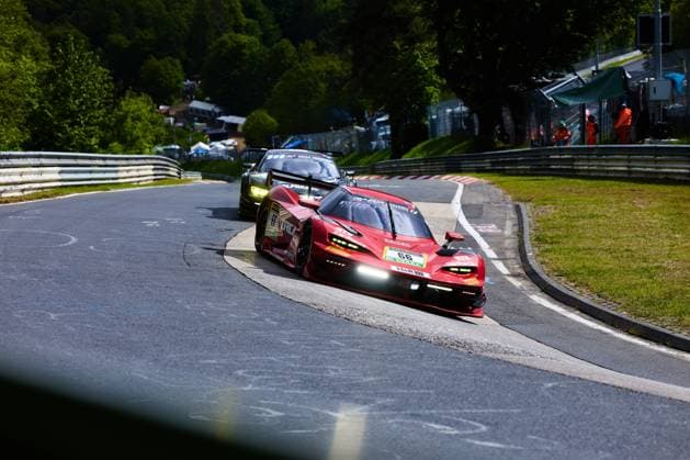 Das rote Fahrzeug mit der Startnummer 66 von Reiter Engineering durchfährt eine enge Kurve auf der Nordschleife am Nürburgring. Mit eingeschalteten Scheinwerfern und H&R-Sponsoring nimmt Arne Hoffmeister & Julien Apotheloz & Laurents Hörr & Marcel Marchewicz & Miklas Born (Reiter Engineering) die Kurve eng, während im Hintergrund ein weiteres GT-Fahrzeug folgt. Streckenposten in orangen Warnwesten sind am Streckenrand zu sehen. Reiter Engineering 66 in der Kurve auf der Nordschleife