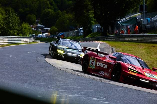 Das rote Fahrzeug mit der Startnummer 66 von Reiter Engineering durchfährt eine enge Kurve auf der Nordschleife am Nürburgring. Auf der Motorhaube und den Flanken sind die Sponsoren ORCA, RAVENOL, ZF und exprotrade gut erkennbar. Dicht dahinter folgt ein dunkles, schwarz-grünes GT3-Fahrzeug mit RAVENOL- und ALPHAZOO-Sponsoring. Im Hintergrund sind Streckenposten in orangefarbener Kleidung und die typische grüne Eifel-Kulisse zu sehen. Arne Hoffmeister & Julien Apotheloz & Laurents Hörr & Marcel Marchewicz & Miklas Born (Reiter Engineering) Reiter Engineering 66 und dunkles GT3-Fahrzeug auf der Nordschleife