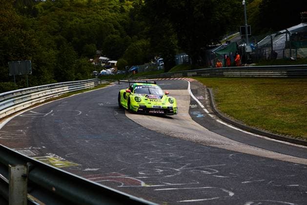 Der markant gelbgrüne Porsche 911 GT3 mit der Startnummer 911 von Manthey durchfährt eine enge Kurve auf der Nordschleife des Nürburgrings beim ADAC RAVENOL 24h Nürburgring 2026. Das mit Red Bull, KÜS und Veltins gesponserte Fahrzeug Ayhancan Güven & Kevin Estre & Thomas Preining (Manthey) nimmt die Kurve präzise, während im Hintergrund Streckenposten in orangefarbener Ausrüstung zu sehen sind. Porsche 911 GT3 911 von Manthey auf der Nordschleife