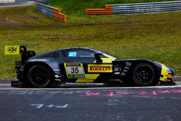 Der Aston Martin AMR GT3 mit der Startnummer 35 von Walkenhorst Motorsport durchfährt eine Kurve auf der Nordschleife beim ADAC RAVENOL 24h Nürburgring. Das schwarz-gelbe Fahrzeug Dennis Fetzer & Felipe Fernandez Laser & Mateo Villagoméz & Stefan Aust (Walkenhorst Motorsport) trägt die Sponsoren Pirelli, RAVENOL und DEKRA prominent auf der Flanke. Im Hintergrund sind die charakteristischen Leitplanken und das grüne Gras der Eifel zu sehen. Walkenhorst Motorsport 35 auf der Nordschleife beim 24h Nürburgring