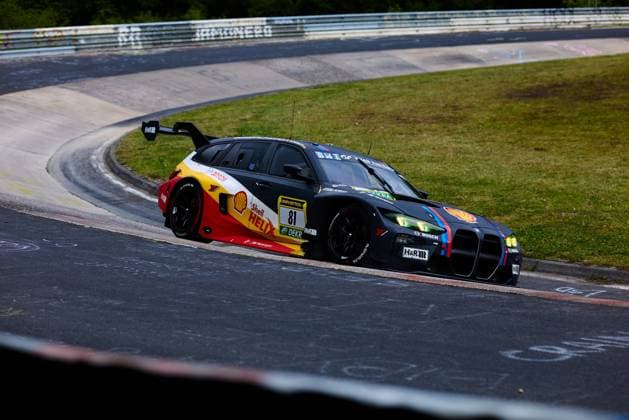 Der BMW M3 GT mit der Startnummer 81 des Teams Schubert Motorsport durchfährt eine enge Kurve auf der Nordschleife am Nürburgring. Das Fahrzeug zeigt das markante Shell Helix-Livery in Schwarz, Rot und Gelb mit den charakteristischen BMW M-Streifen. Sponsoren wie Shell, RAVENOL, H&R und Bosch sind deutlich auf der Karosserie zu erkennen. Connor de Phillippi & Jens Klingmann & Neil Verhagen & Ugo de Wilde (BMW M Motorsport) BMW M3 GT 81 von Schubert Motorsport in der Nordschleife-Kurve