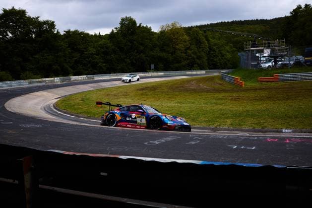 Der Porsche 911 GT3 mit der Startnummer 4 des Teams Goroyan RT by Car Collection durchfährt eine Kurve auf der Nordschleife am Nürburgring. Das Fahrzeug Alex Fontana & Artur Goroyan & Nathanael Berthon & Oleg Kivtka & Oleg Kvitka (Goroyan RT by Car Collection) trägt ein auffälliges blau-rot-orangefarbenes Livery mit den Sponsoren GInvest und SRT. Im Hintergrund ist die charakteristische Streckenführung der Nordschleife mit Leitplanken und Gr NFL, American Football Herren, USA chen zu erkennen. Porsche 911 GT3 4 von Goroyan RT by Car Collection auf der Nordschleife
