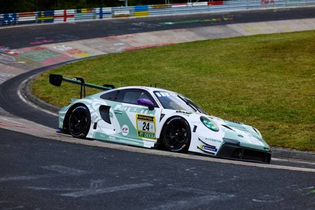 Der Porsche 911 GT3 R mit der Startnummer 24 durchfährt eine Kurve auf der Nordschleife des Nürburgrings. Das Fahrzeug 24; TSV Schleißheim präsentiert sich in einem auffälligen mintgrün-weißen Farbschema mit dem Sponsor PATENTIA und RAVENOL-Nummerntafel. Michelin-Reifen und das DEKRA-Logo sind deutlich erkennbar. Im Hintergrund sind die charakteristischen bunten Kreidezeichnungen der Fans auf dem Curb sichtbar. Porsche 911 GT3 R 24 von Manthey auf der Nordschleife