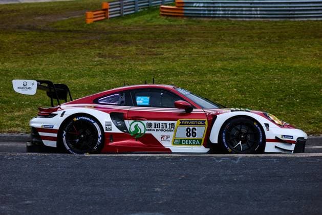 Der Porsche 911 GT3 mit der Startnummer 86 von High Class Racing durchfährt eine Kurve auf dem Nürburgring. Das rot-weiße Fahrzeug Anders Fjordbach & Hongli Ye & Kerong Li & King Harry (High Class Racing) trägt die Sponsoren Derun Environment, RAVENOL und DEKRA prominent auf der Karosserie. Michelin-Reifen und das charakteristische Heckflügel-Setup des GT3-Rennwagens sind gut erkennbar. Porsche 911 GT3 86 von High Class Racing auf dem Nürburgring