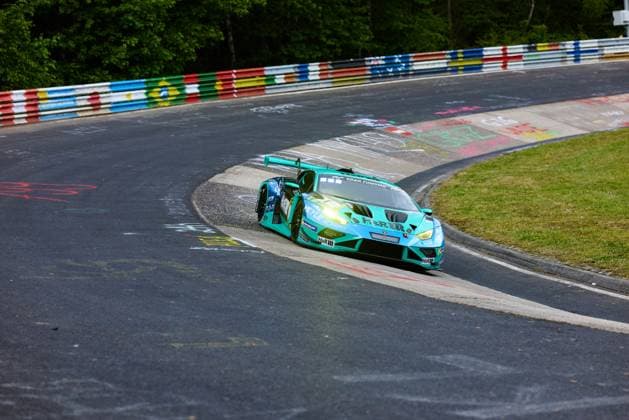 Der türkisfarbene Lamborghini Huracán GT3 mit der Startnummer 91 von Reiter Engineering durchfährt eine enge Kurve auf der Nordschleife des Nürburgrings. Das Fahrzeug mit den Sponsoren H&R und MEYLE ist in einer dynamischen Kurvenfahrt zu sehen, während im Hintergrund die typischen bunten Leitplanken der Nordschleife und dichte Bäume das Bild prägen. Lukas Ertl & Matthias Benndorf & Maximilian Johannes Ertl & Stefan Ertl (Reiter Engineering) Lamborghini Huracán GT3 91 von Reiter Engineering in der Nordschleife-Kurve