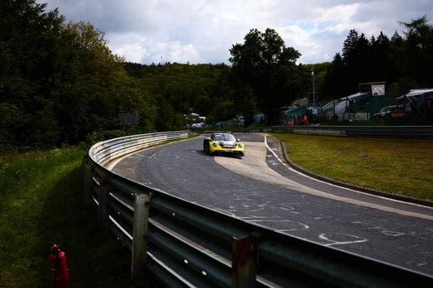 Der gelbe Porsche 911 GT3 mit der Startnummer 91 von Reiter Engineering durchfährt eine langgezogene Kurve auf der Nordschleife des Nürburgrings. Lukas Ertl & Matthias Benndorf & Maximilian Johannes Ertl & Stefan Ertl (Reiter Engineering) Die charakteristische grüne Vegetation der Eifel und die typischen Leitplanken der Nordschleife prägen das Bild. Im Hintergrund sind Streckenposten in orangefarbener Kleidung sowie Zuschauerbereich zu erkennen. Gelber Porsche 911 GT3 91 von Reiter Engineering auf der Nordschleife