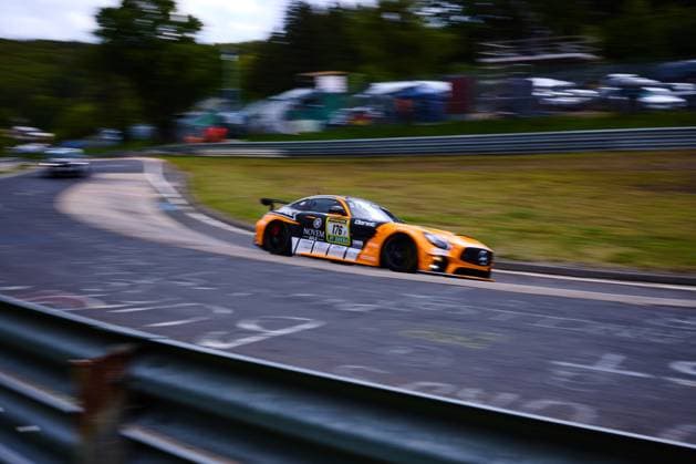 Der orangefarbene Mercedes-AMG GT3 mit der Startnummer 176 von PROsport Racing durchfährt mit hoher Geschwindigkeit eine Kurve auf dem Nürburgring. Das Fahrzeug Abée Anton & Guilherme de Oliveira & Jörg Viebahn & LLuc Ibanez & Yannik Himmels (PROsport Racing) zeigt deutlich die Sponsoren NOVEM Gold und RAVENOL auf der Karosserie. Die Panning-Aufnahme betont die Dynamik des Rennwagens vor dem unscharfen Hintergrund der Nordschleife. Mercedes-AMG GT3 176 von PROsport Racing auf dem Nürburgring