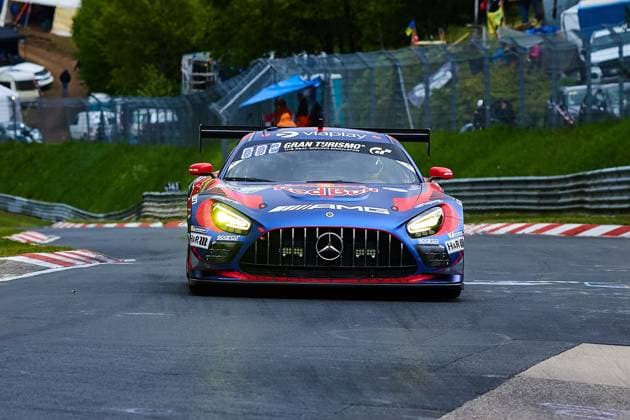Der Mercedes-AMG GT3 mit der Startnummer 3 des Mercedes-AMG Team Verstappen Racing durchfährt eine Kurve auf der Nordschleife des Nürburgrings. Das in Blau und Rot gehaltene Fahrzeug trägt die Sponsoren Red Bull, Viaplay und Gran Turismo prominent auf der Karosserie und ist mit eingeschalteten Scheinwerfern unterwegs. Daniel Juncadella & Jules Gounon & Lucas Auer & Max Verstappen (Mercedes-AMG Team Verstappen Racing) zeigt sich in einer frontalen Perspektive mit dem charakteristischen Mercedes-Stern im Kühlergrill. Mercedes-AMG GT3 3 von Mercedes-AMG Team Verstappen Racing auf der Nordschleife