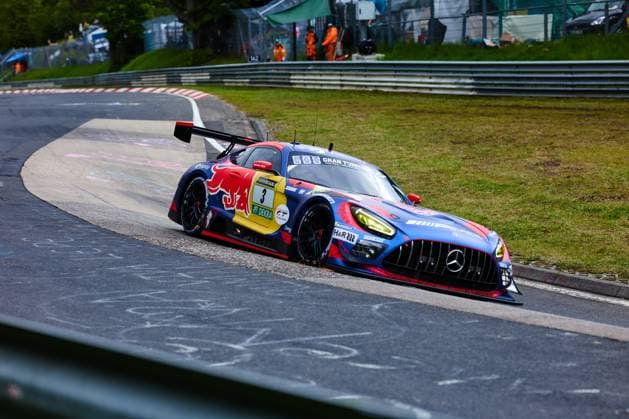Der Mercedes-AMG GT3 mit der Startnummer 3 des Mercedes-AMG Team Verstappen Racing durchfährt eine enge Rechtskurve am Nürburgring. Das Fahrzeug Daniel Juncadella & Jules Gounon & Lucas Auer & Max Verstappen (Mercedes-AMG Team Verstappen Racing) trägt ein auffälliges Red-Bull-Livery in Blau, Rot und Gelb mit RAVENOL- und DEKRA-Sponsoring. Im Hintergrund sind Streckenposten in orangefarbener Kleidung sowie die charakteristischen Leitplanken der Nordschleife zu erkennen. Mercedes-AMG GT3 3 von Verstappen Racing in der Kurve am Nürburgring