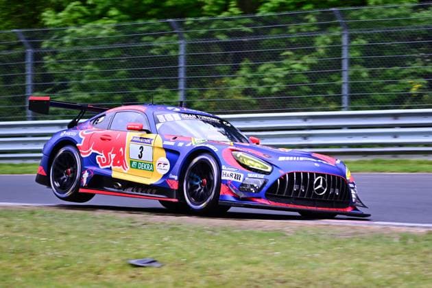 Der Mercedes-AMG GT3 mit der Startnummer 3 des Mercedes-AMG Team Verstappen Racing durchfährt eine Kurve auf dem Nürburgring. Das Fahrzeug Daniel Juncadella & Jules Gounon & Lucas Auer & Max Verstappen (Mercedes-AMG Team Verstappen Racing) trägt ein markantes Red-Bull-Livery in Blau, Rot und Gelb und ist mit Sponsoren wie RAVENOL, DEKRA und H&R versehen. Die Aufnahme zeigt das Fahrzeug in schneller Fahrt auf der Nordschleife, umgeben von grüner Vegetation und Leitplanken. Mercedes-AMG GT3 3 von Verstappen Racing auf der Nordschleife Copyright: xMichaelxGelhardtx