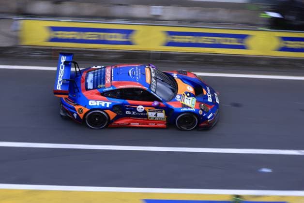 Der Porsche 911 GT3 R mit der Startnummer 4 von Goroyan RT by Car Collection durchquert die Boxengasse am Nürburgring. Das Fahrzeug Alex Fontana & Artur Goroyan & Nathanael Berthon & Oleg Kivtka & Oleg Kvitka (Goroyan RT by Car Collection) trägt ein markantes blau-orange-rotes Farbschema mit den Sponsoren GRT, GInvest, RAVENOL und Falken. Im Hintergrund ist die charakteristische Castrol-Werbebande sichtbar. Porsche 911 GT3 R 4 von Goroyan RT by Car Collection auf dem Nürburgring