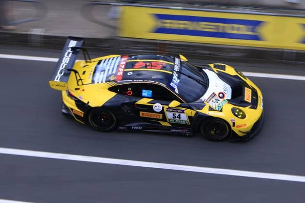 Der Porsche 911 GT3 R mit der Startnummer 54 des Teams Dinamic GT durchfährt die Boxengasse am Nürburgring. Das Fahrzeug präsentiert sich im markanten schwarz-gelben Design mit Sponsoren wie Ravenol, Pirelli und Wempe. Bastian Buss & Michael Christensen & Michael Klitgaard Christensen (Dinamic GT) Porsche 911 GT3 R 54 von Dinamic GT in der Boxengasse