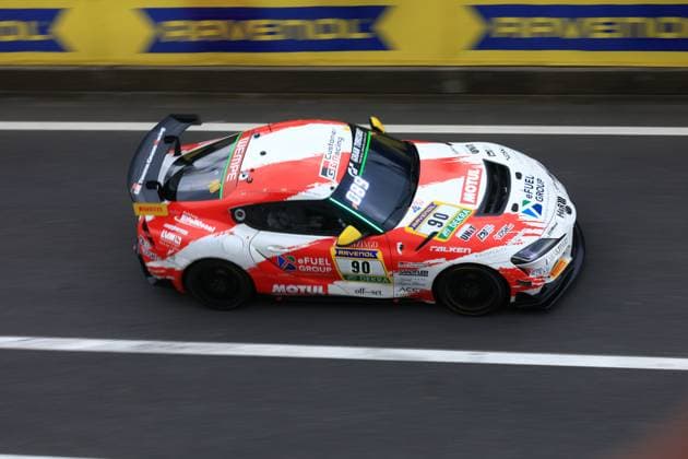 Der Hugo Schwarze & Javier Sagrera (Toyota Racing United) von Toyota Racing United durchfährt die Boxengasse am Nürburgring. Das rot-weiße Fahrzeug mit der Startnummer 90 trägt die Sponsoren MOTUL, eFUEL GROUP, RAVENOL und FALKEN und ist mit einem markanten Heckflügel ausgestattet. Im Hintergrund ist das RAVENOL-Banner entlang der Streckenabsperrung zu erkennen. Ferrari GT3 90 von Toyota Racing United auf dem Nürburgring
