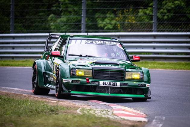 Der Mercedes-Benz 190E Evo von HWA Engineering Speed (Adam Adelson & James Green & Lance David Arnold & Renger Van der Zande (HWA Engineering Speed)) nimmt eine Kurve auf der Nordschleife des Nürburgrings. Das dunkelgrüne Fahrzeug mit markanten gelben Scheinwerfern trägt die Startnummer 63 und ist mit Sponsoren wie Parkside, H&R, Hankook und Gran Turismo versehen. Das Fahrzeug zeigt eine beeindruckende Breitspur-Karosserie mit großem Heckflügel und tief abgestimmtem Fahrwerk. Mercedes 190E Evo 63 von HWA Engineering Speed auf der Nordschleife Copyright: xMichaelxGelhardtx
