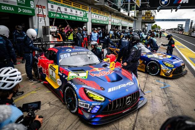 Der Mercedes-AMG GT3 Daniel Juncadella & Jules Gounon & Lucas Auer & Max Verstappen (Mercedes-AMG Team Verstappen Racing) von Mercedes-AMG Team Verstappen Racing steht in der Boxengasse des Nürburgrings für einen Boxenstopp. Das Fahrzeug trägt das markante Red-Bull-Livery in Blau, Rot und Gold mit prominenten Sponsoren wie Red Bull, Viaplay, Gran Turismo, RAVENOL, Falken und AMG. Die Mechaniker in blauen Teamoveralls arbeiten konzentriert am Fahrzeug, während im Hintergrund ein zweites Fahrzeug — der blau-goldene Falken Motorsports Mercedes-AMG GT3 44 — ebenfalls bedient wird. Zahlreiche Fotografen und Teammitglieder säumen die geschäftige Boxengasse, im Hintergrund sind Sponsorenbanner von DEKRA, ADAC, RAVENOL und Hyundai zu sehen. Mercedes-AMG GT3 3 von Verstappen Racing beim Boxenstopp am Nürburgring Copyright: xMichaelxGelhardtx