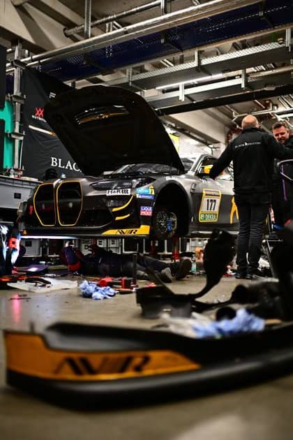 Der McLaren GT3 Alexandru Vasilescu & David Ogburn & Malcolm Harrison & Mark Smith & Sergiu Nicolae (AV Racing by BLACK FALCON) von AV Racing by BLACK FALCON steht in der beleuchteten Box am Nürburgring. Das Fahrzeug in charakteristischer schwarz-gelber Lackierung wird von Mechanikern in BLACK FALCON-Teamkleidung betreut. Sponsoren wie LIQUI-MOLY und DEKRA sind am Fahrzeug sichtbar. Die Aufnahme zeigt die nächtliche Atmosphäre eines Langstreckenrennens. McLaren 177 von AV Racing by BLACK FALCON in der Box am Nürburgring Copyright: xMichaelxGelhardtx
