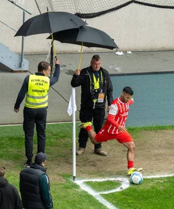 FUSSBALL REGIONALLIGA NORDOST 34. SPIELTAG FC CARL ZEISS JENA - FC ROT WEISS ERFURT ** NUR FÜR REDAKTIONELLE ZWECKE ** EDITORIAL USE ONLY **<p>16 05 2026-Jena: Fussball Regionalliga Nordost 34. Spieltag Saison 2025-2026 Ernst-Abbe-Sportfeld FC Carl Zeiss Jena - FC Rot Weiss Erfurt im Foto: Sejdo Durakov 54 (FC Rot‘Weiß Erfurt) wird beim Eckball von Ordnern mit Schirmen geschützt. ( Deutschland Thueringen Jena Copyright: SaschaxFromm