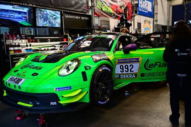 Der Björn Griesemann & Dirk Adorf & Georg Griesemann & Marco Holzer (Manthey Team eFuel Griesemann) steht in der Boxengarage am Nürburgring. Das markant grün lackierte Fahrzeug von Manthey Team eFuel Griesemann trägt die Startnummer 992 und ist mit Sponsoren wie RAVENOL, LeFuels, Griesemann und H&R prominent beklebt. Im Hintergrund sind Monitore, Werkzeug und weiteres Boxen-Equipment zu sehen. Das Fahrzeug ist auf roten Aufstellböcken positioniert, während Teammitglieder an der Box arbeiten. Porsche 911 GT3 R 992 von Manthey Team eFuel Griesemann in der Box Copyright: xMichaelxGelhardtx