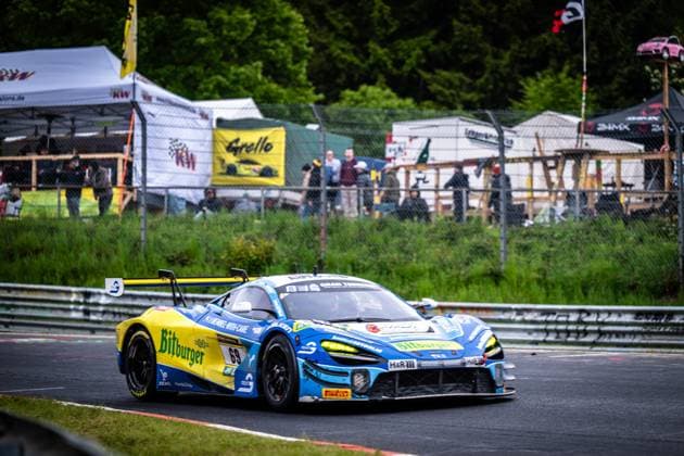 Der McLaren GT3 mit der Startnummer 69 von Doerr Motorsport durchfährt eine Kurve auf dem Nürburgring. Das Fahrzeug trägt das markante gelb-blaue Bitburger-Livery und ist mit Sponsoren wie H&R und Falken ausgestattet. Im Hintergrund sind Zuschauerbereich sowie Werbebanner von KW und Grello zu sehen. Ben Doerr & Marvin Kirchhöfer & Timo Glock & Timo Scheider (Doerr Motorsport) McLaren GT3 69 von Doerr Motorsport auf dem Nürburgring Copyright: xMichaelxGelhardtx