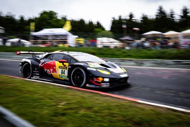 Der Lamborghini Huracán GT3 Luca Engstler & Mirko Bortolotti & Patric Niederhauser (Red Bull Team ABT) von Red Bull Team ABT durchfährt mit hoher Geschwindigkeit eine Kurve am Nürburgring. Das schwarz-gelbe Fahrzeug mit Red Bull-Livery und der Startnummer 84 ist in einer dynamischen Panning-Aufnahme festgehalten, wobei der Hintergrund mit Zuschauern und Zelten in Bewegungsunschärfe verschwimmt. Gut sichtbare Sponsoren sind Red Bull und RAVENOL. Lamborghini 84 von Red Bull Team ABT am Nürburgring Copyright: xMichaelxGelhardtx
