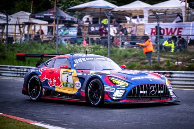 Der Mercedes-AMG GT3 3 von Mercedes-AMG Team Verstappen Racing durchfährt eine Kurve auf der Nordschleife am Nürburgring. Das Fahrzeug trägt das markante Red-Bull-Livery in Blau, Rot und Gelb mit auffälligem Red-Bull-Logo auf der Fahrzeugflanke. Sponsoren wie RAVENOL, Viaplay, DEKRA und Gran Turismo sind prominent auf der Karosserie zu sehen. Im Hintergrund sind Streckenposten sowie Zuschauer und Hospitality-Zelte erkennbar, darunter ein Banner mit dem Schriftzug ROWE. Daniel Juncadella & Jules Gounon & Lucas Auer & Max Verstappen (Mercedes-AMG Team Verstappen Racing) Mercedes-AMG GT3 3 von Verstappen Racing auf der Nordschleife Copyright: xMichaelxGelhardtx