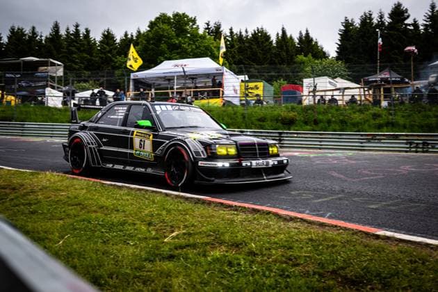 Der markante schwarze Mercedes-Benz mit der Startnummer 61 von HWA Engineering Speed nimmt die Kurve auf dem Nürburgring. Das aufwendig gestaltete Fahrzeug mit charakteristischer schwarzer Lackierung, roten Bremsscheiben und gelben Scheinwerfern zeigt eine aggressive aerodynamische Karosserie. Sponsoren wie RAVENOL und DEKRA sind gut sichtbar. Im Hintergrund sind Zuschauer, Zelte und gelbe Fahnen zu erkennen, die die Atmosphäre des 24h Nürburgring 2026 unterstreichen. Bruno Spengler & Christian Gebhardt & Evald Holstad & Peter Ludwig (HWA Engineering Speed) Mercedes-Benz 61 von HWA Engineering Speed auf dem Nürburgring Copyright: xMichaelxGelhardtx