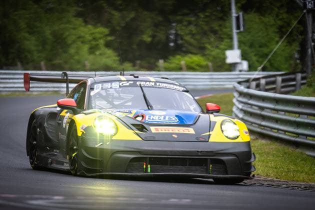 Der Porsche 911 GT3 R Lukas Ertl & Matthias Benndorf & Maximilian Johannes Ertl & Stefan Ertl (Reiter Engineering) von Reiter Engineering durchfährt eine Kurve auf der Nordschleife am Nürburgring. Das Fahrzeug in charakteristischer schwarz-gelber Farbgebung mit blauem Dach ist mit leuchtenden Scheinwerfern unterwegs. Deutlich sichtbar sind die Sponsoren Endless und Pirelli auf der Karosserie. Im Hintergrund sind die typischen Leitplanken und die grüne Vegetation der Eifel zu sehen. Porsche 911 GT3 R 91 von Reiter Engineering auf der Nordschleife Copyright: xMichaelxGelhardtx